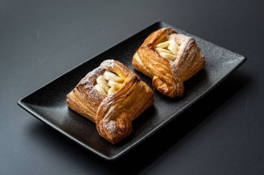 Tatlı, siyah arka planda siyah servis tabağına doldurulmuş küçük bir börek turtasıdır. Kesilmiş bir parça kek.