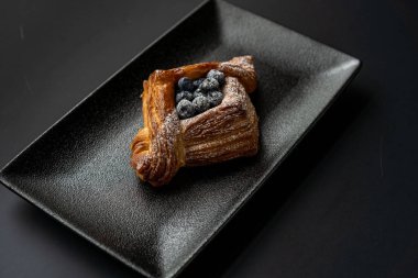 Tatlı, siyah arka planda siyah servis tabağına doldurulmuş küçük bir börek turtasıdır. Kesilmiş bir parça kek.