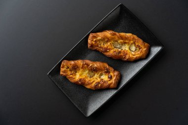 Tatlı, siyah arka planda siyah servis tabağına doldurulmuş küçük bir börek turtasıdır. Kesilmiş bir parça kek.