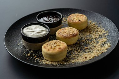 Ekşi kremalı ve reçelli siyah tabakta süzme peynirli kek.