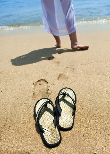 Beach slippers on sand, and female feet at a sea edge — Stock Photo, Image