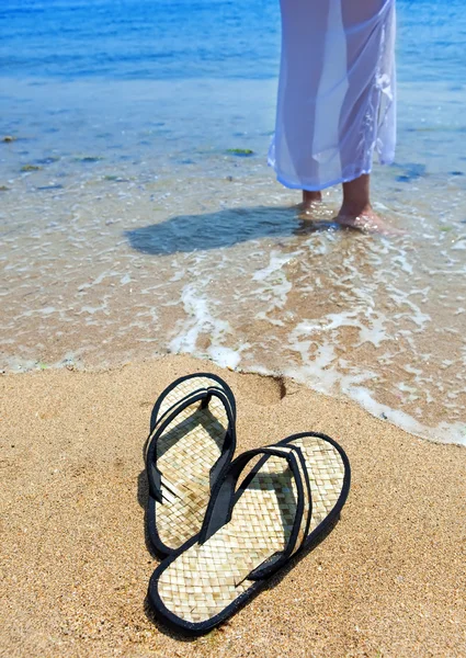 Pantoufles de plage sur sable, et pieds femelles au bord de la mer — Photo