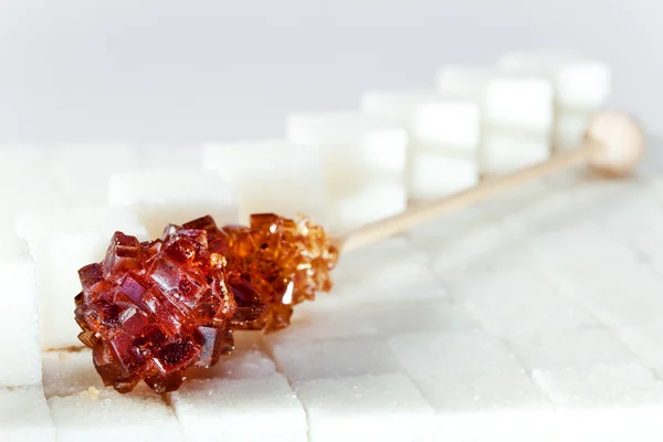 Candy brown sugar on a stick lies on white lumpy sugar — Stock Photo, Image