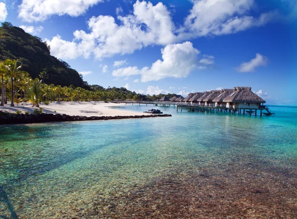 Typisch polynesische Landschaft - Meeresküste mit Palmen und kleinen Häusern am Wasser. — Stockfoto