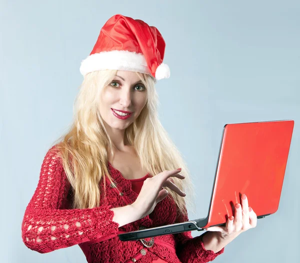 Güzel sarışın genç kadın kırmızı dizüstü bilgisayar ile bir yılbaşı şapkalı — Stok fotoğraf