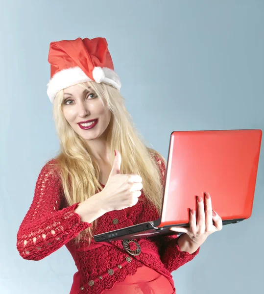 Den unga vackra blonda kvinnan i ett nytt år hatt med röd laptop visar en tumme — Stockfoto