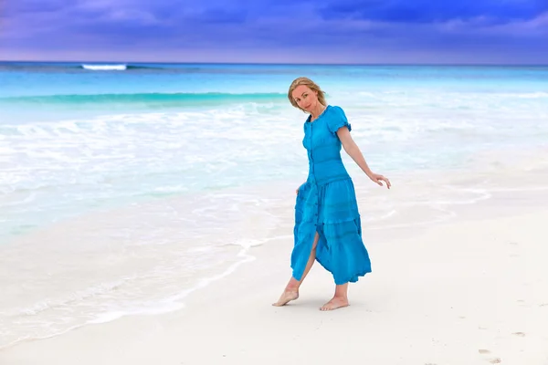 Женщина в длинном голубом платье на бурном морском побережье — стоковое фото