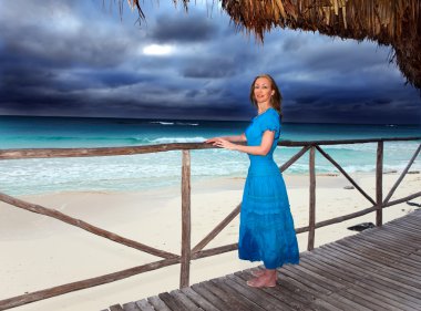 fırtınalı deniz kıyısında uzun mavi elbiseli kadına