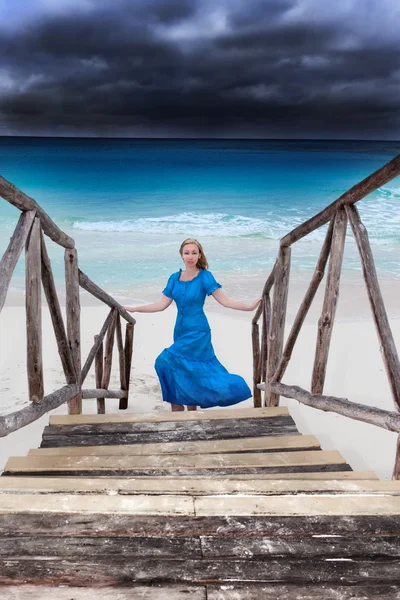 A mulher em um vestido azul longo vai na costa do mar tempestuosa — Fotografia de Stock