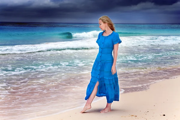 A mulher em um vestido azul longo vai na costa do mar tempestuosa — Fotografia de Stock