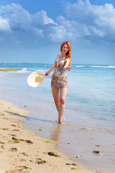Jovem mulher bonita vai na costa do oceano com chapéu de palha nas mãos — Fotografia de Stock