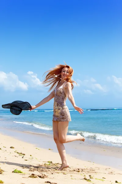 Mladá žena jde na pobřeží oceánu s kloboukem — Stock fotografie