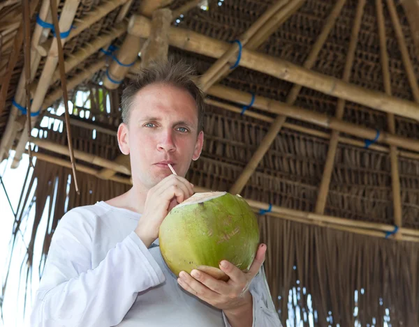 Attractive man drinks coconut juice from a nut on a beach at the sea — Stock Photo, Image