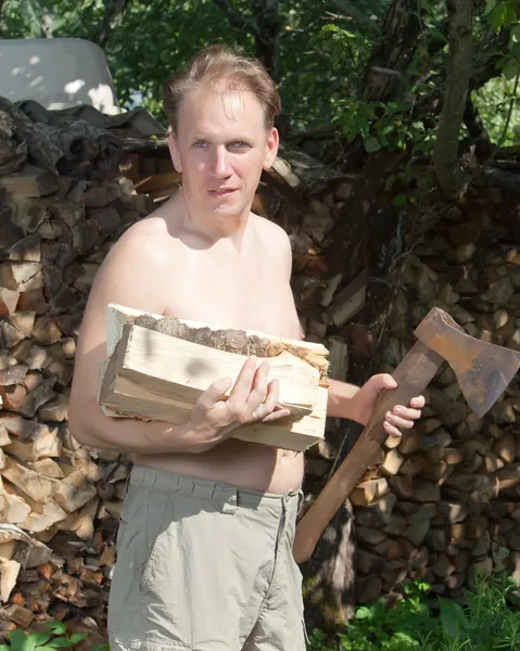 El hombre con un hacha que parte prepara leña para calentar la casa. — Foto de Stock