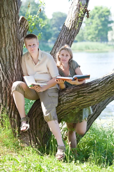 Joven chico y la chica se preparan para las lecciones, examen en el parque de primavera cerca del lago — Foto de Stock