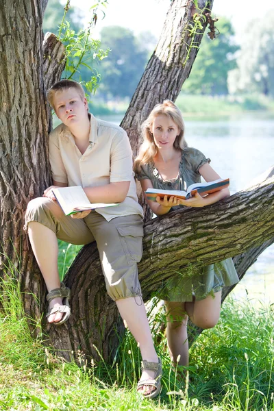 Joven chico y la chica se preparan para las lecciones, examen en el parque de primavera cerca del lago — Foto de Stock