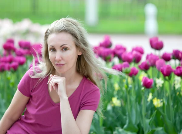 Die junge schöne Frau im Frühlingspark mit blühenden Tulpen — Stockfoto