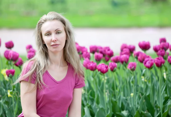 A jovem mulher bonita no parque de primavera com tulipas florescentes — Fotografia de Stock