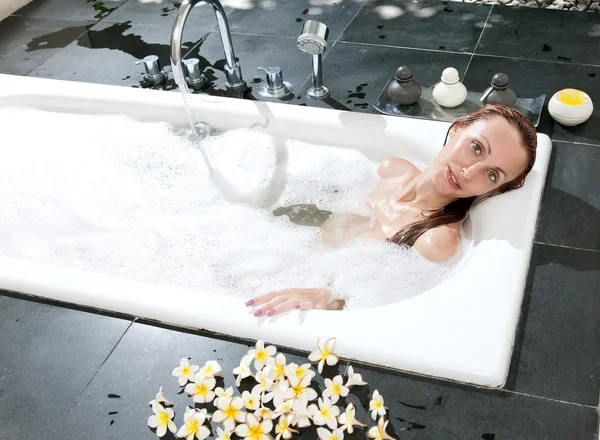 La mujer se acuesta en jabones en el baño, agua llena —  Fotos de Stock
