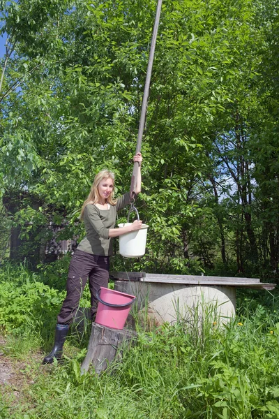 Mladá žena u studny, nalévá vodu do vědra — Stock fotografie