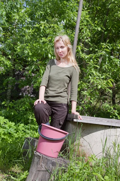 A fiatal nő a kútnál vizet önt egy vödörbe. — Stock Fotó
