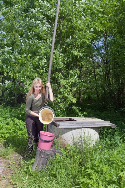 La jeune femme à un puits verse de l'eau dans un seau — Photo