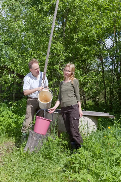 Mladý šťastný pár na studny, Lije vodu do kbelíku — Stock fotografie