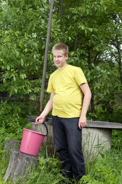 Der Junge, der Teenager, gießt Wasser in einen Eimer aus einem Brunnen — Stockfoto