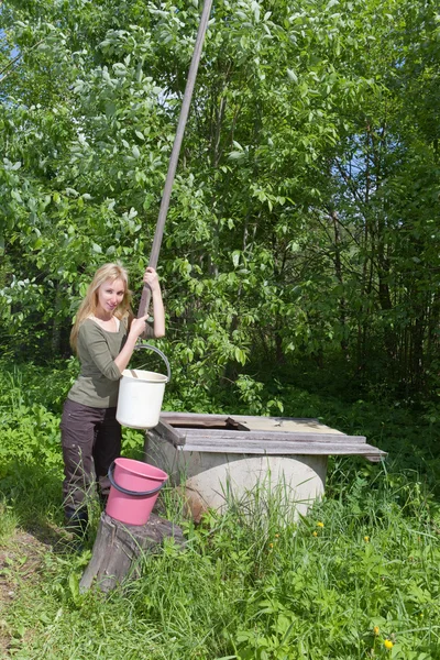 Die junge Frau an einem Brunnen gießt Wasser in einen Eimer — Stockfoto