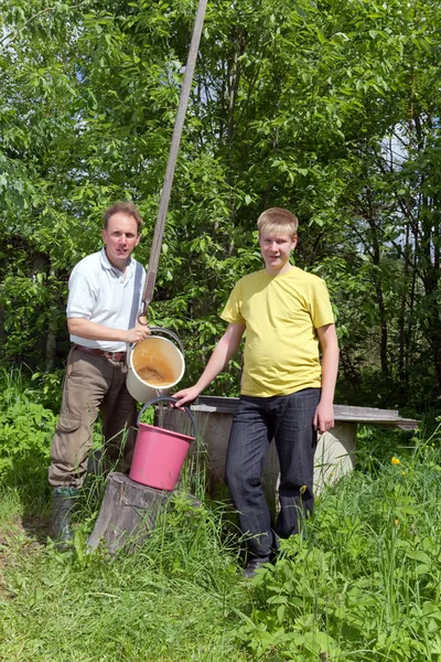 Le garçon aide le père à verser de l'eau dans un seau d'un puits — Photo