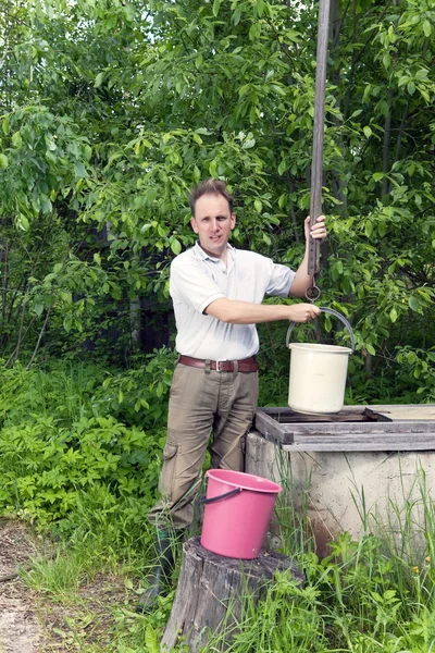 Man at a well, pours water in a bucket — Stock Photo, Image