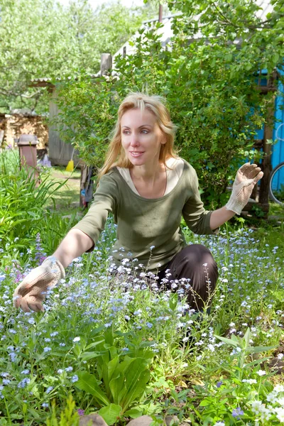 Jonge mooie vrouw ziet er na achter planten in de tuin — Stockfoto