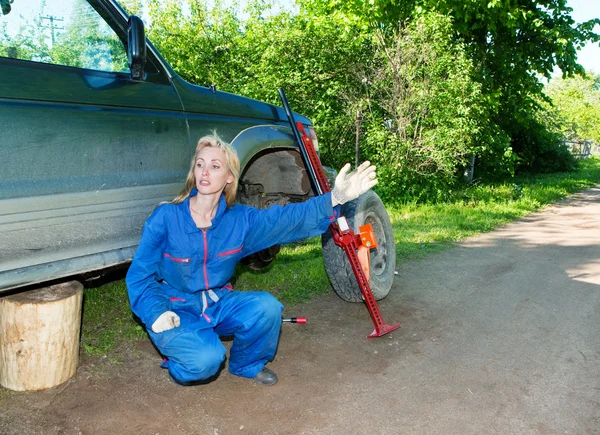 Женщина в рабочем комбинезоне пытается заменить колесо внедорожника — стоковое фото
