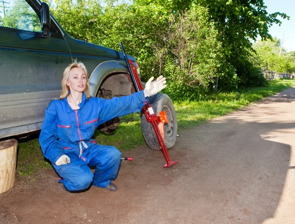 The woman in working overalls tries to replace a wheel at an off-road car — Stock Photo, Image