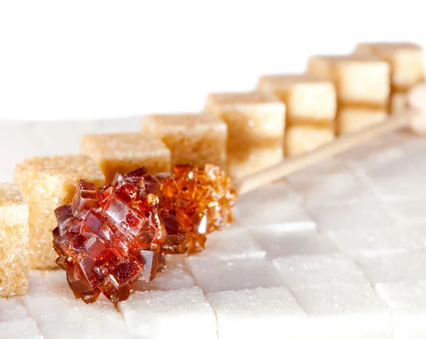 Sladký hnědý cukr na tyčince leží na hrudkovitém cukru — Stock fotografie