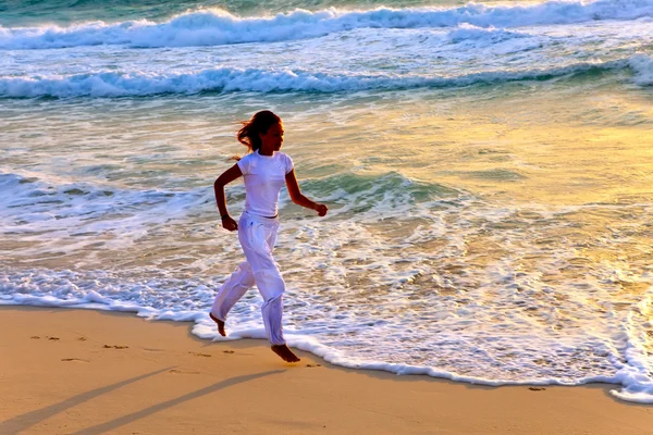 석양에 바다의 가장자리를 따라 실행 하는 여자의 실루엣 — 스톡 사진