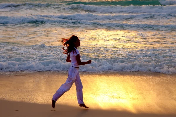 Silueta de mujer corriendo a lo largo del borde del mar en una puesta de sol — Foto de Stock