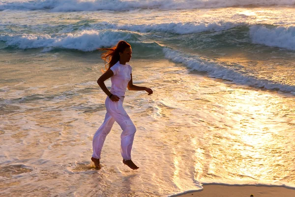 Silhueta de mulher correndo ao longo da borda do mar em um sunse — Fotografia de Stock