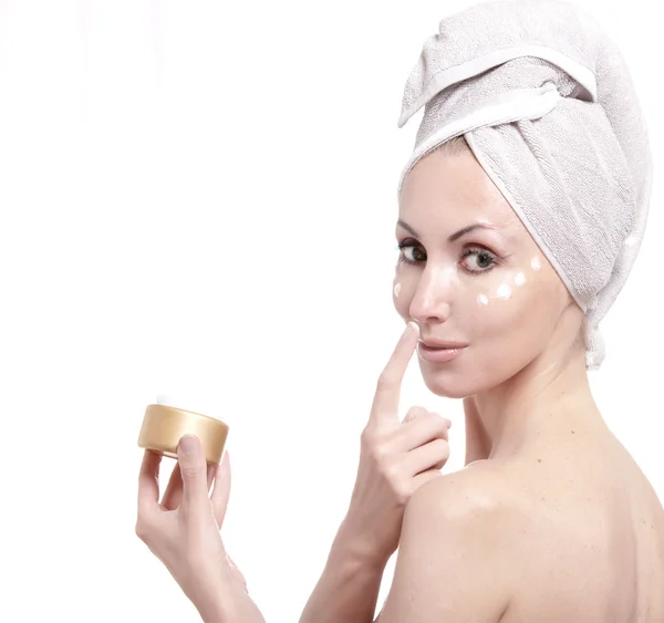 De mooie jonge vrouw in de handdoek met een cosmetische crème — Stockfoto