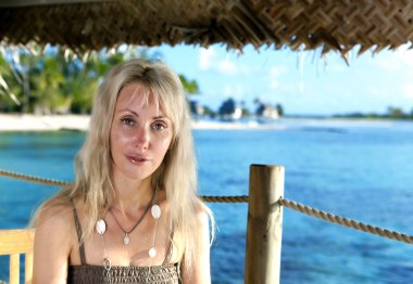 güzel bir kadın denizde gerdanlı bir gölgelik altında oturur.