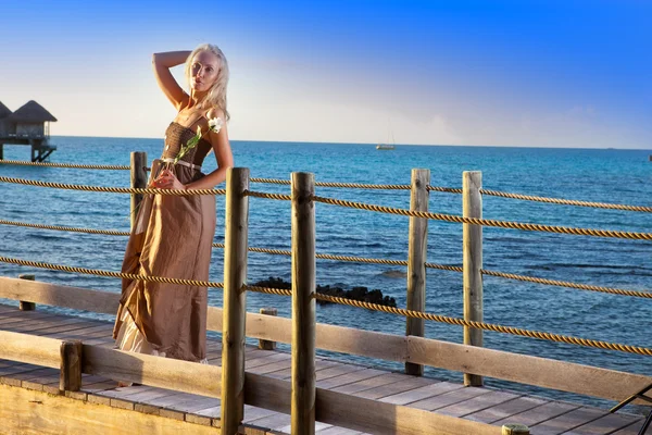 La joven hermosa mujer en un vestido largo en el camino de madera sobre el mar —  Fotos de Stock