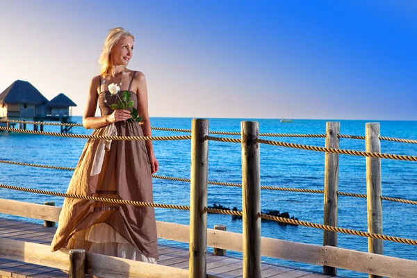 La joven hermosa mujer en un vestido largo en el camino de madera sobre el mar — Foto de Stock