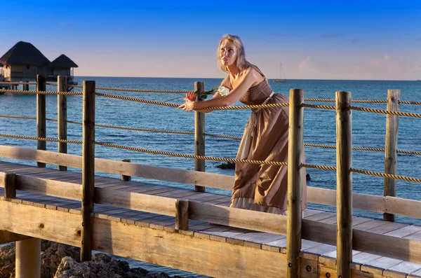 A jovem mulher bonita em um vestido longo na estrada de madeira sobre o mar — Fotografia de Stock