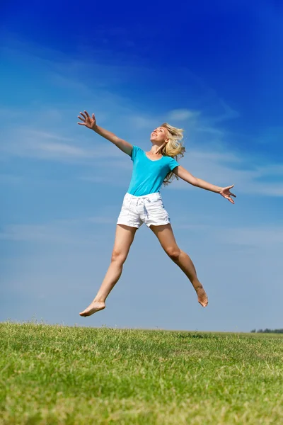 La mujer feliz salta en un campo verde de verano contra el cielo azul —  Fotos de Stock