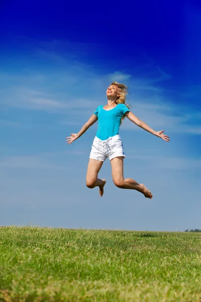 The happy woman jumps in a summer green field against the blue sky Stock Picture