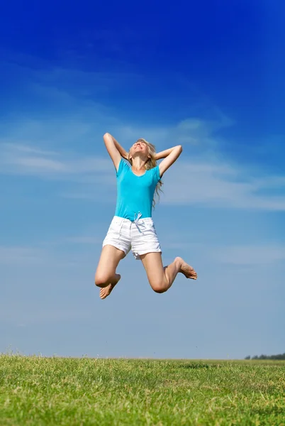 Die glückliche Frau springt in ein sommergrünes Feld gegen den blauen Himmel Stockfoto