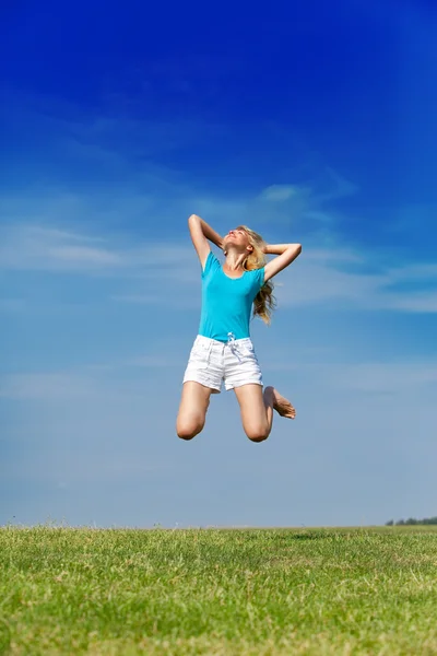 The happy woman jumps in a summer green field against the blue sky Stock Image