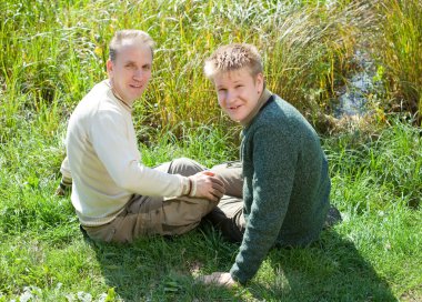 Baba ile oğlu çimenli göl kıyısında oturmak