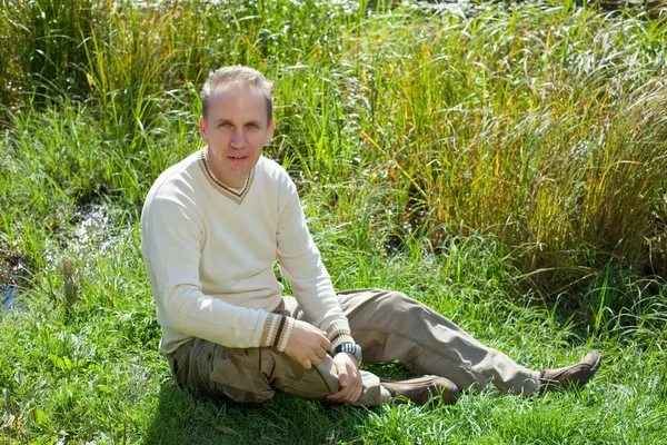 Мужчина сидит в траве на берегу озера — стоковое фото