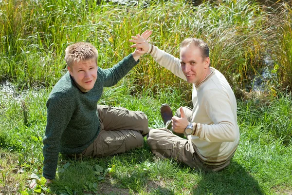 Le père avec le fils assis sur la côte herbeuse du lac — Photo